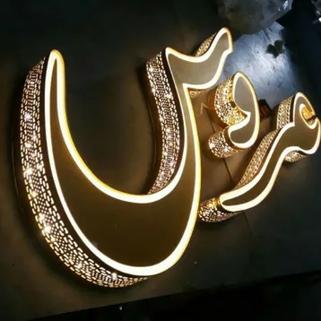 كلمة عربية بأحرف ذهبية بارزة تنعكس إضاءتها الخلفية على الجدار