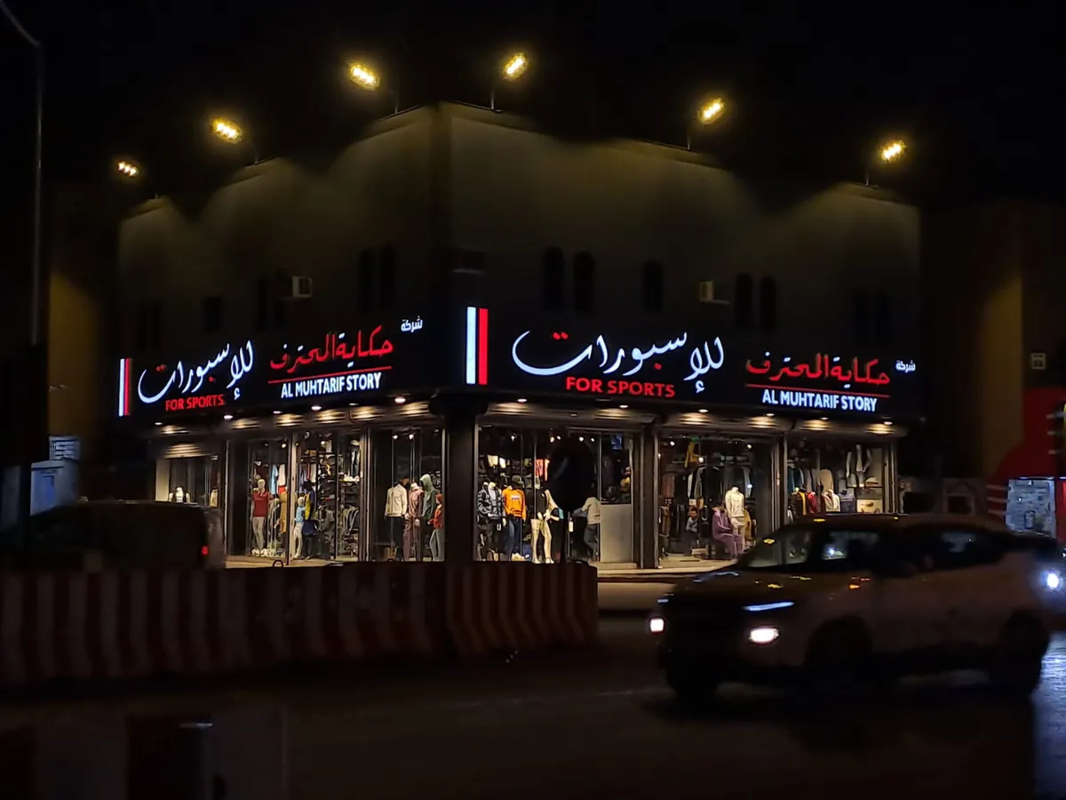 لوحات متجر حكاية المحترف للإسبورات على واجهتين بأحرف عربية وإنجليزية مضيئة ليلاً