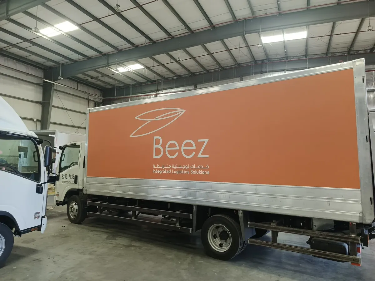 شاحنة بصندوق مغلّف باللون البرتقالي وشعار Beez داخل مستودع