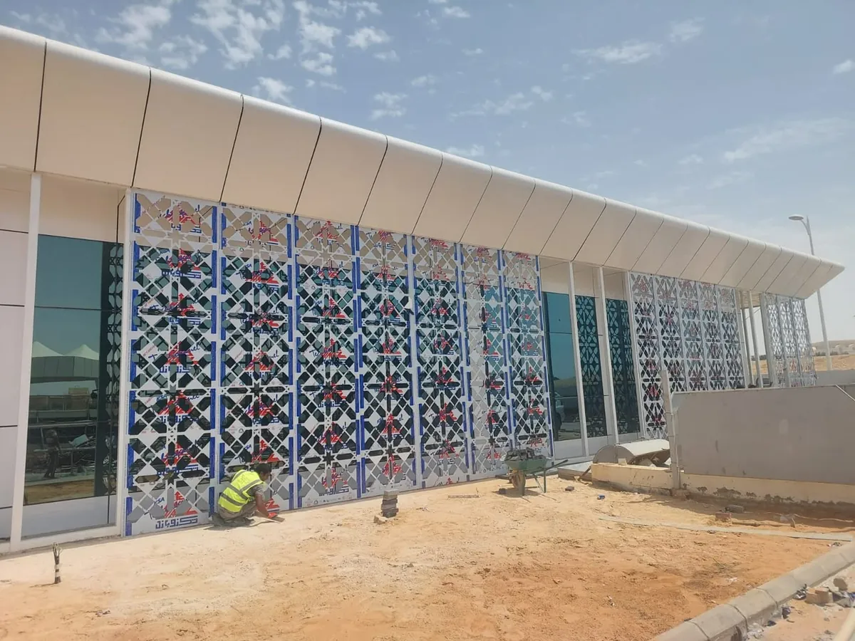 سواتر مخرّمة بنقوش هندسية إسلامية أمام واجهة زجاجية تعلوها مظلة بيضاء منحنية أثناء التركيب