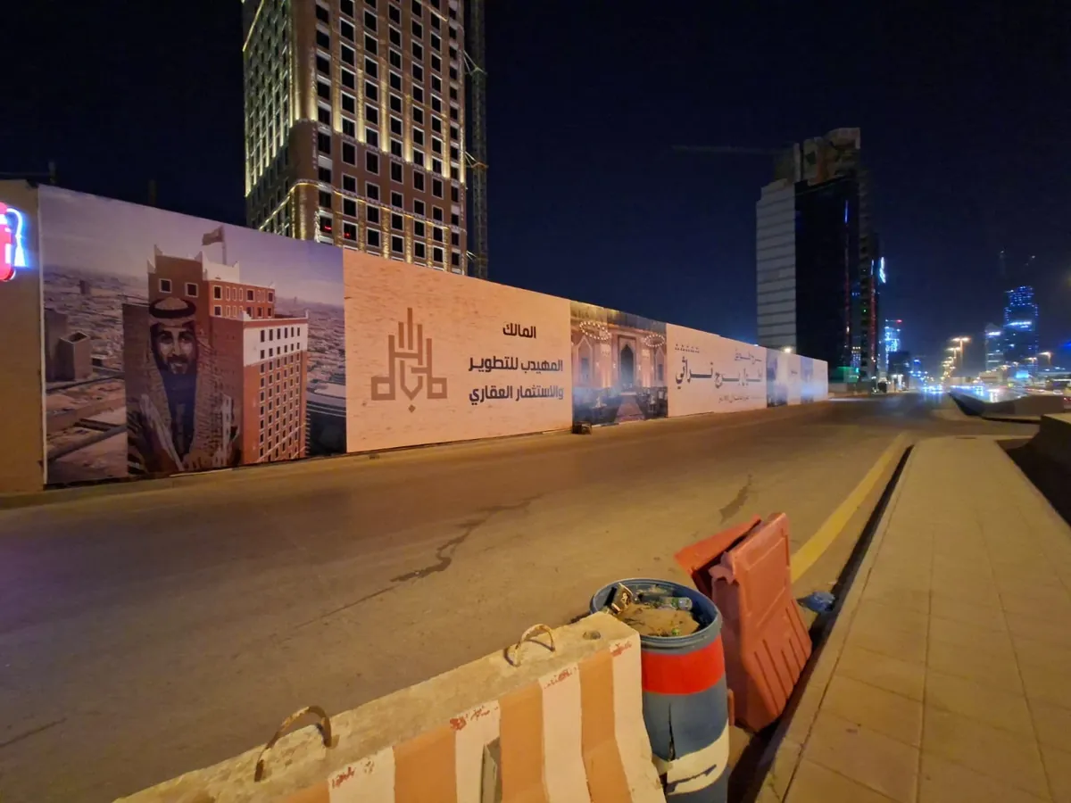 سور مشروع المهيدب للتطوير والاستثمار العقاري بطباعة ملوّنة على امتداد الطريق ليلاً
