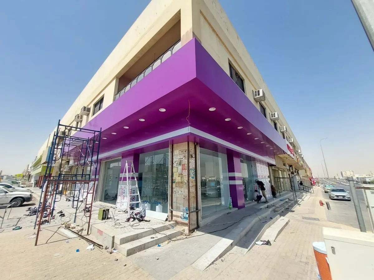 واجهة ركنية لمحلات تجارية مكسوّة بألواح كلادينج بنفسجية مع إضاءة سبوت